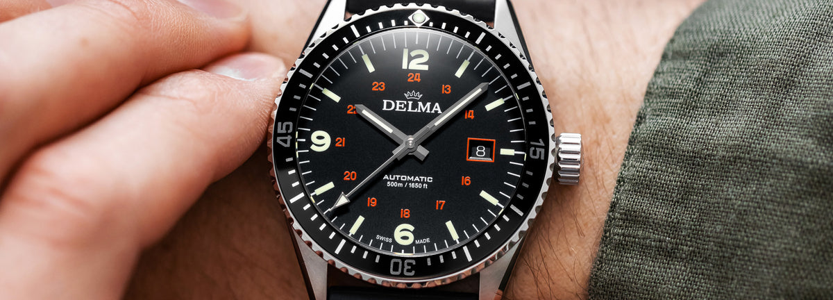 DELMA Cayman Field stainless steel watch with black dial and black rubber strap on wrist