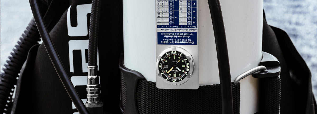 DELMA Quattro stainless steel watch with black dial and black bezel on decompression plate with dive gear