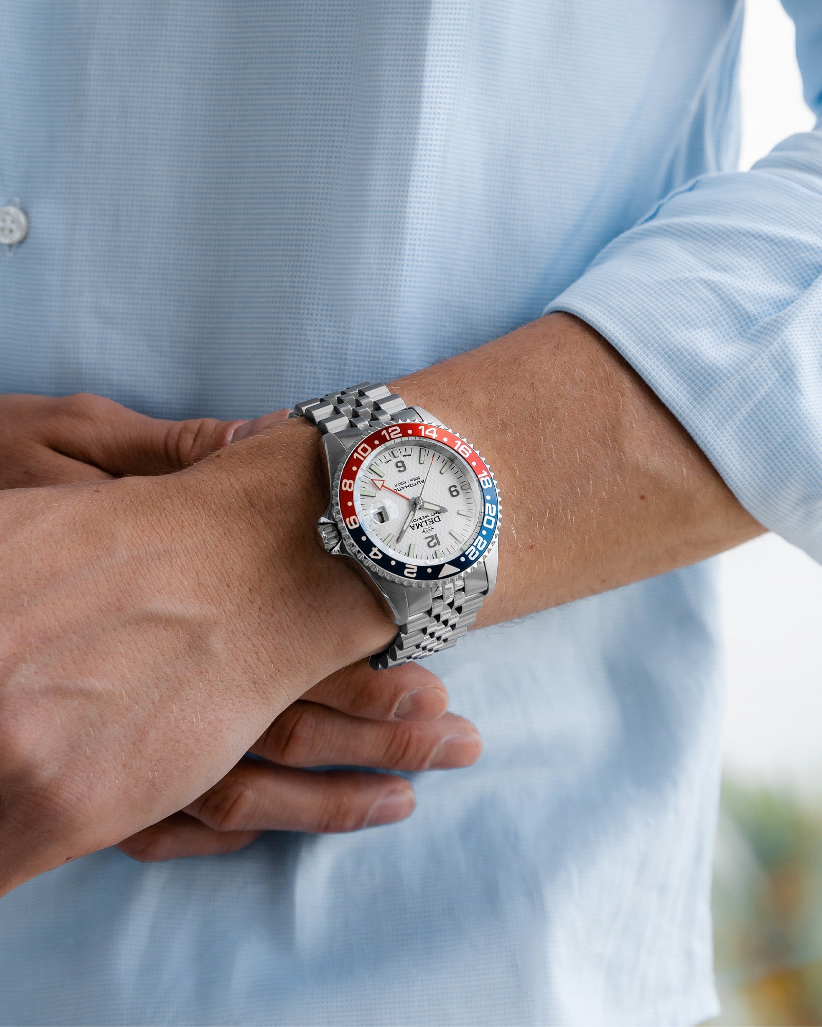 DELMA Santiago GMT Meridian Automatic stainless steel watch with white dial and blue and red bezel on wrist