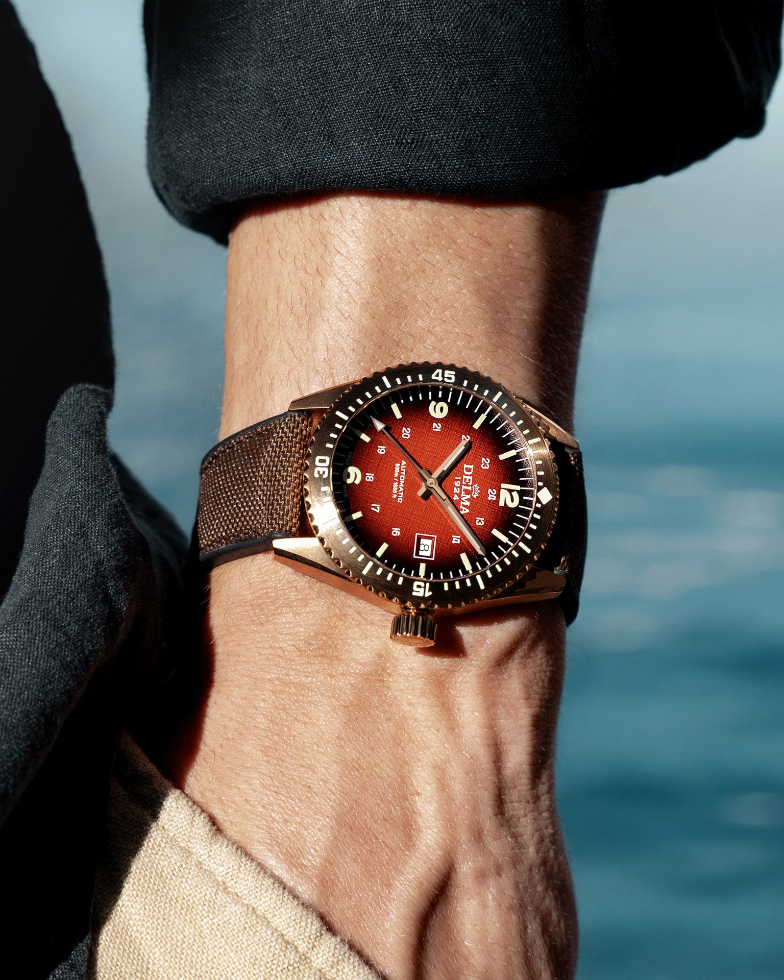 DELMA Cayman Bronze watch with red gradient dial and brown Cordura strap on wrist