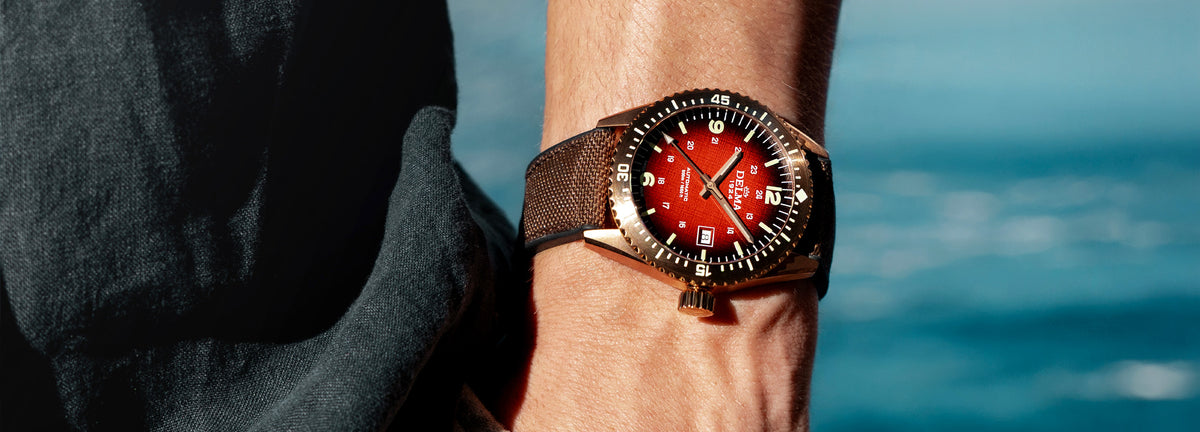 DELMA Cayman Bronze watch with red gradient dial and brown Cordura strap on wrist