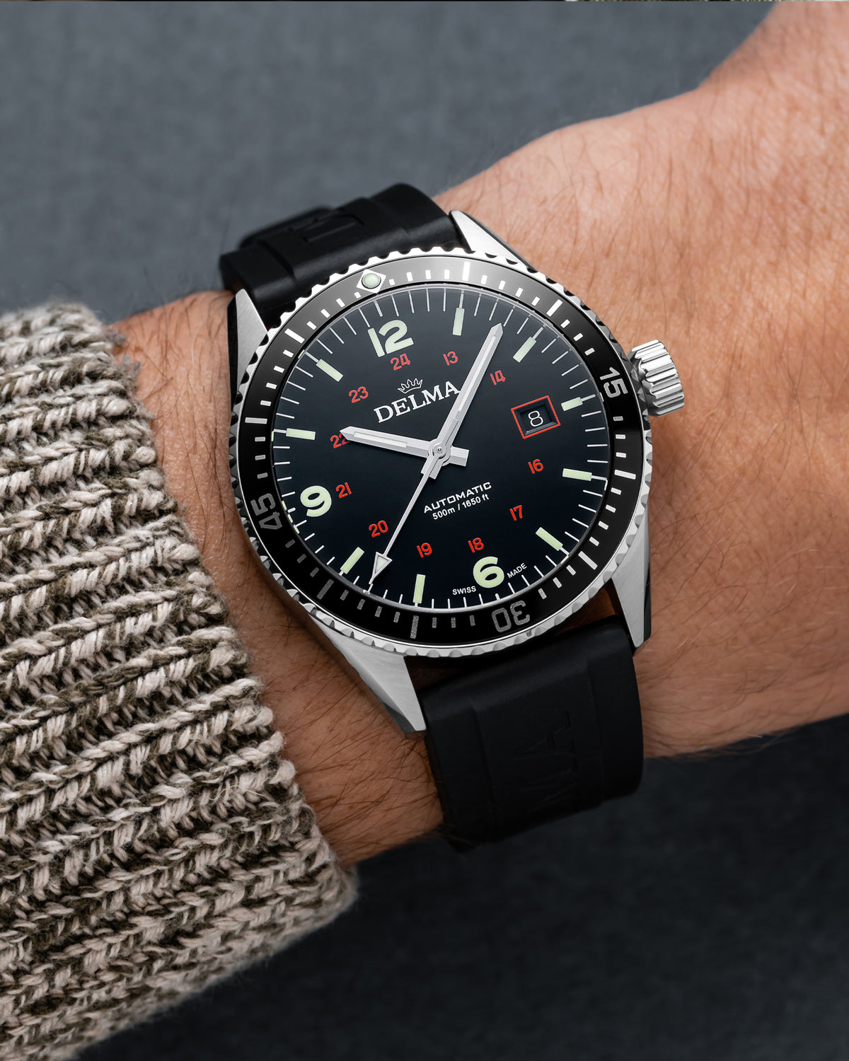 DELMA Cayman Field stainless steel watch with black dial and black rubber strap on wrist