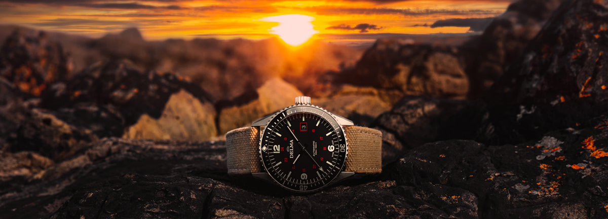 DELMA Cayman Field stainless steel watch with black dial and khaki color canvas strap in context sunset