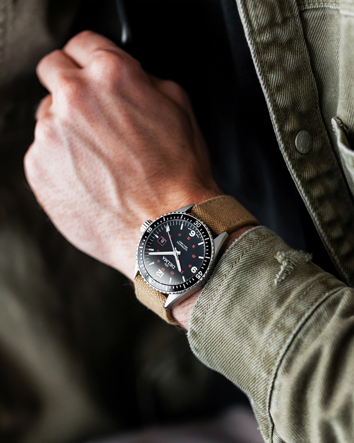 DELMA Cayman Field stainless steel watch with black dial and khaki color canvas strap on wrist