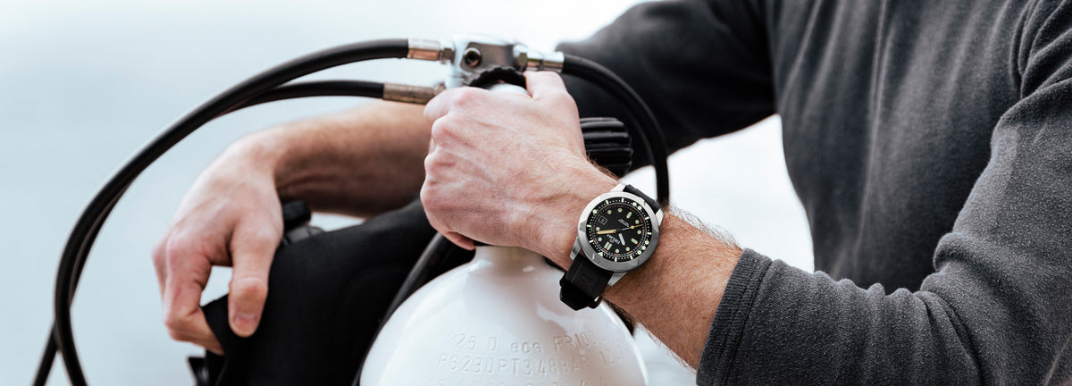DELMA Quattro stainless steel watch with black dial and black bezel on wrist with dive gear